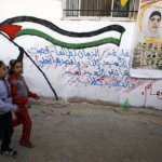 Children walk past a poster welcoming freed Palestinian prisoners in Qalandiya refugee camp near the West Bank city of Ramallah, October 19, 2011. REUTERS/Eric Gaillard