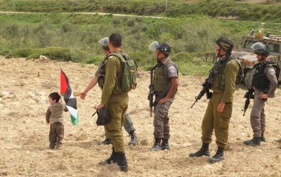 A young boy holds a Palestinian flag in front of Israeli soldiers 