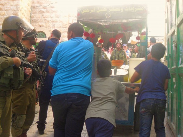 Palestinians try to take a juice stall through the souq, blocked by settlers and soldiers - (Photo by ISM)