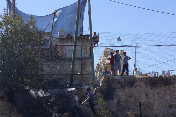 Israeli settler children stand laughing on the partially scorched wall just above their untouched plot of illegally cultivated land (Photo by Christian Peacemaker Teams)