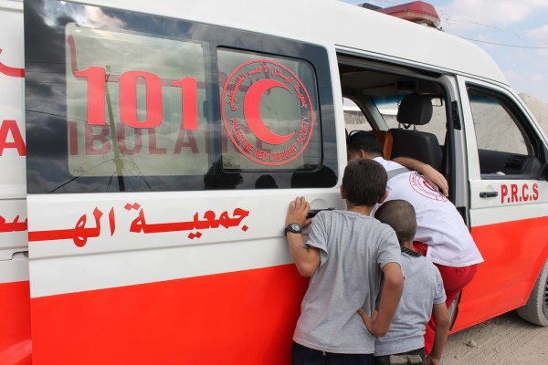 Boys watch as Palestinian Red Crescent Society medics help a demonstrator suffering from tear gas inhalation into an ambulance. (Photo by Joe Catron)