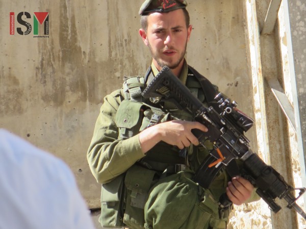 Heavily-armed Israeli soldier closely watching Palestinians pass on their way home from Prayer