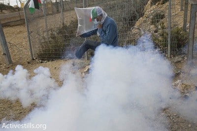 A Palestinian man kicks a tear gas grenade, shot by Israeli soldiers, during a mach against the apartheid wall in the West Bank village of Bi'lin, on January 1, 2010.