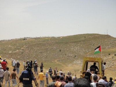 Bulldozer working Palestinian land accompanied by peaceful protesters. Illegal settlement outpost visible on hill 