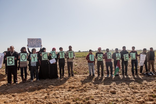 Palestinian and international activists hold signs in support of the Boycott, Divestment and Sanctions (BDS) movement by the buffer zone in Zeitoun on 9 February 2013.