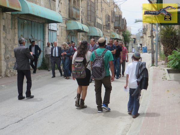 The delegation on Shuhada Street, with Shuada checkpoint in the background and a group of settlers passing them
