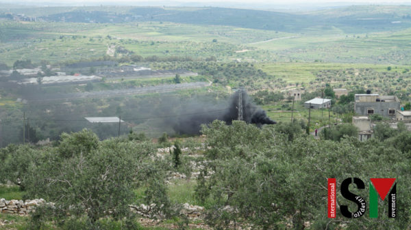 protesters on hill, black smoke blowing towards settlement