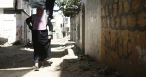 A Palestinian woman walking down a small street in Jenin. The ground is full of rubble.