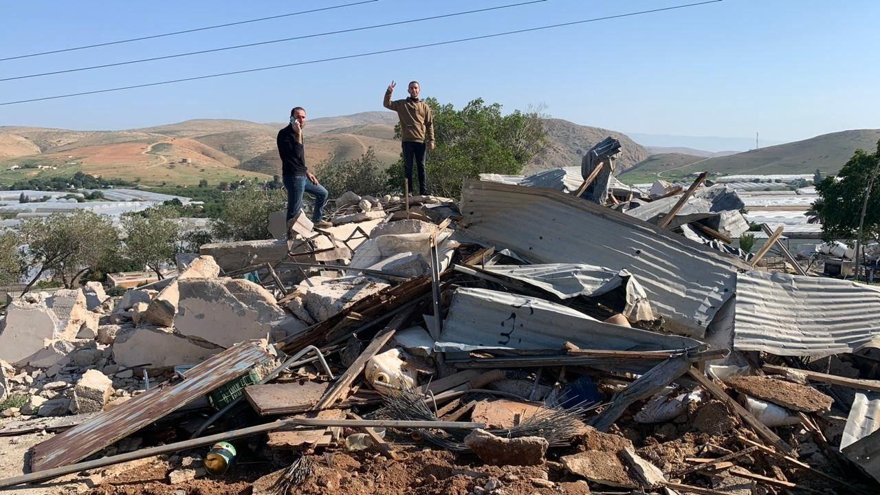 A large heap of rubble and metal. Two men are standing on it, one looking to the camera and doing a peace sign.