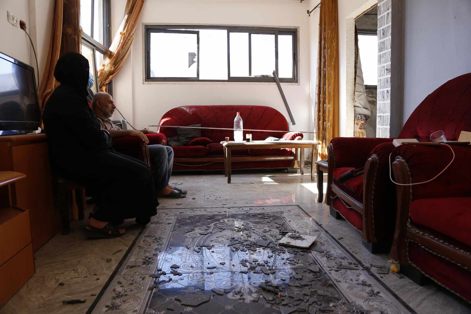 A resident of Nour Shams sits amongst shrapnel strewn inside his home after the Israeli bombardment