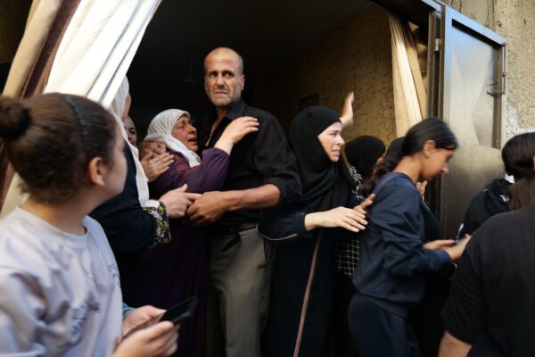 A Palestinian woman is crying and being held by a Palestinian man. Around them, a crowd of women and girls are making their way to the funeral march.