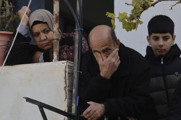 A man, a woman and a boy are standing by a wall, looking defeated. The woman is leaning on the wall, the man is holding his head in his hands.