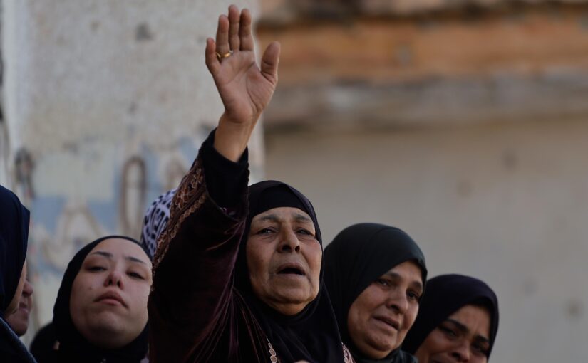 Four Palestinian women are portrayed from the shoulders up, all crying. The one in the centre is raising her arm in a farewell motion.