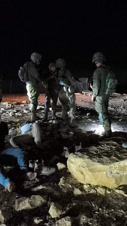 Armed soldiers detain Palestinian man seated on the ground and and blindfolded