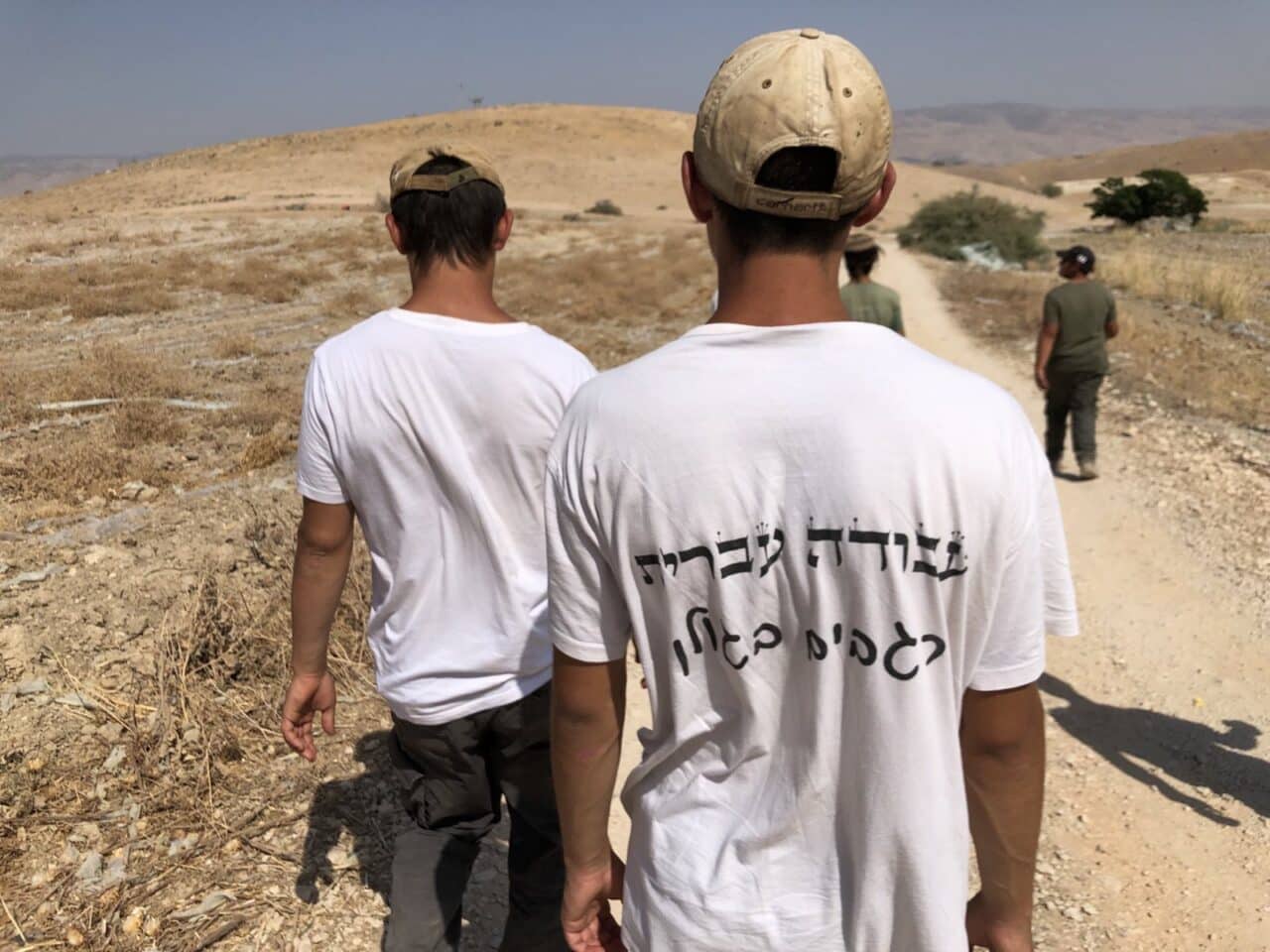Two young men wearing shirts with Hebrew lettering walk away from the camera