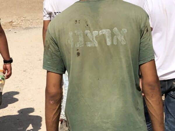 A man wearing a shirt with Hebrew lettering walks away from the camera.
