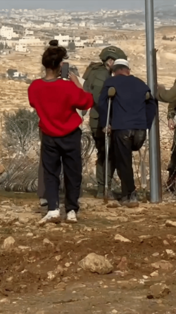 Photo: Shaikh Said is seen from behind watching, standing on crutches, as Israeli armed forces destroy the boundary fence he'd built around his property